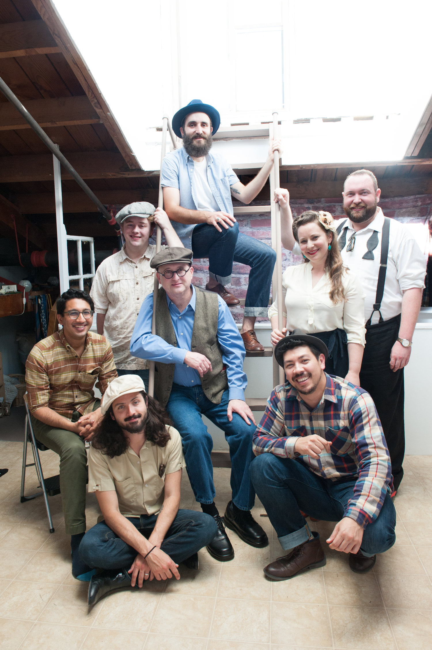 Eight musicians smiling and posing under a sunny skylight.