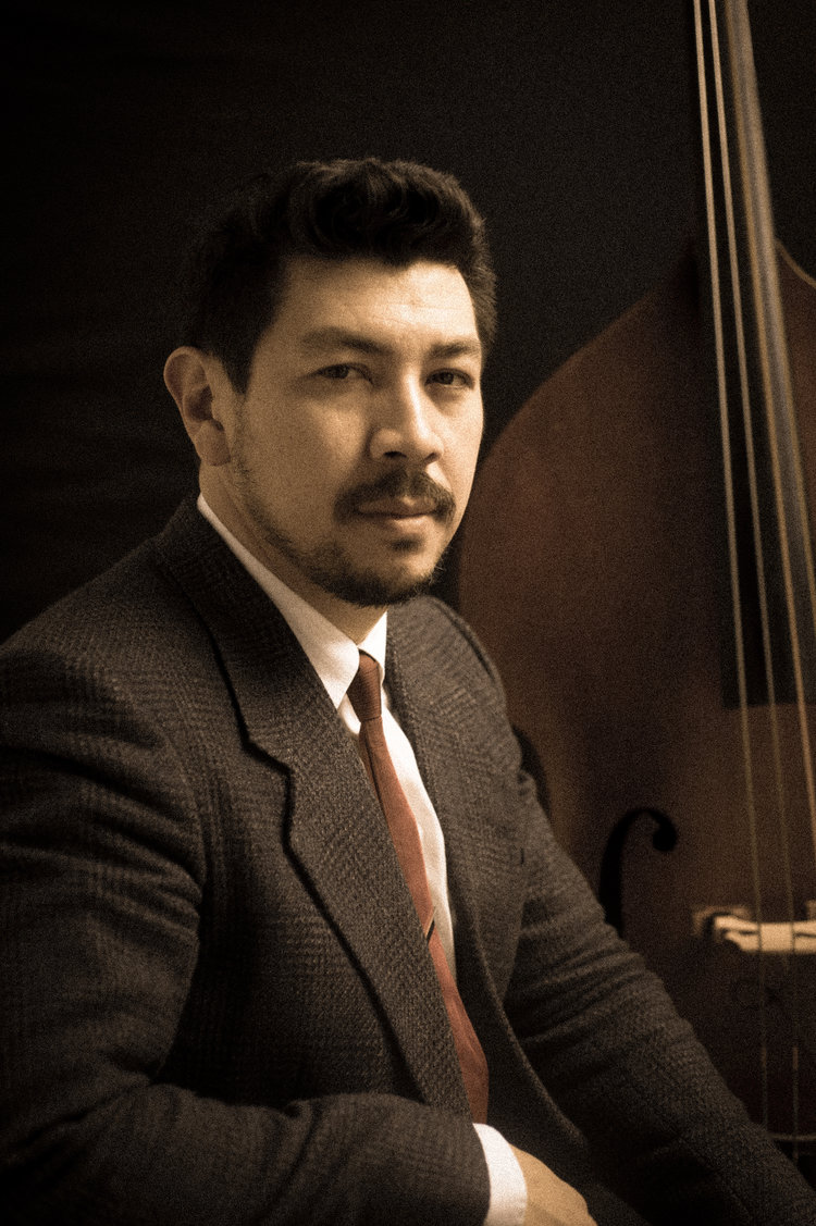 A mustachioed man sitting in front of an upright bass.