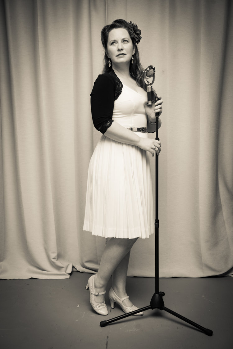 A woman standing with a vintage-looking microphone on a stand.