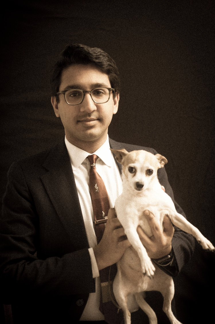 A man in a suit holding a small dog aloft.